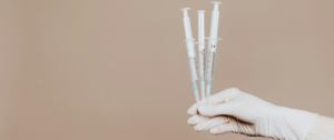 A person holding three medical syringes filled with colorful liquid medications, against a white background.