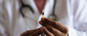 A close-up of a person's hand holding a medical syringe with a clear liquid, against a blurred background.