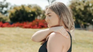 Woman outdoors holding her shoulder and wincing in pain.
