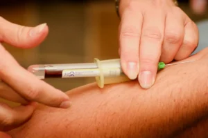 Healthcare professional drawing blood from a patient's arm using a syringe and collection tube.