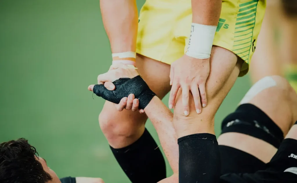 A rugby player in yellow helping an opponent in black off the ground, grasping their hand wrapped in black athletic tape during a match